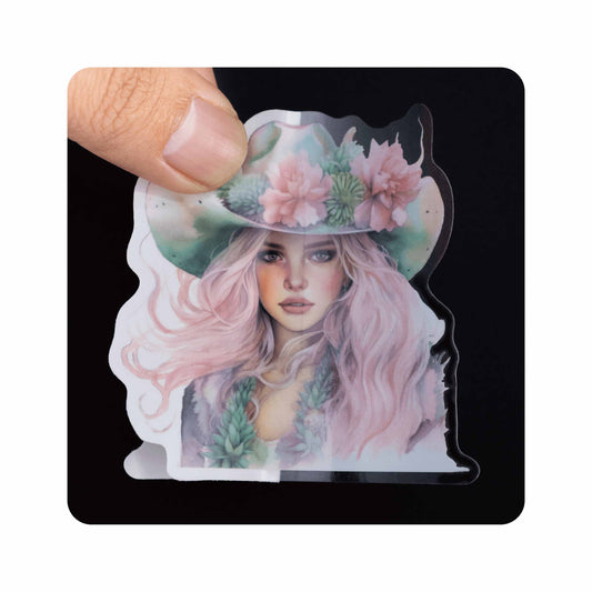Clear transparent die‑cut vinyl sticker, cowgirl portrait design, no white background, hand‑held sample display.