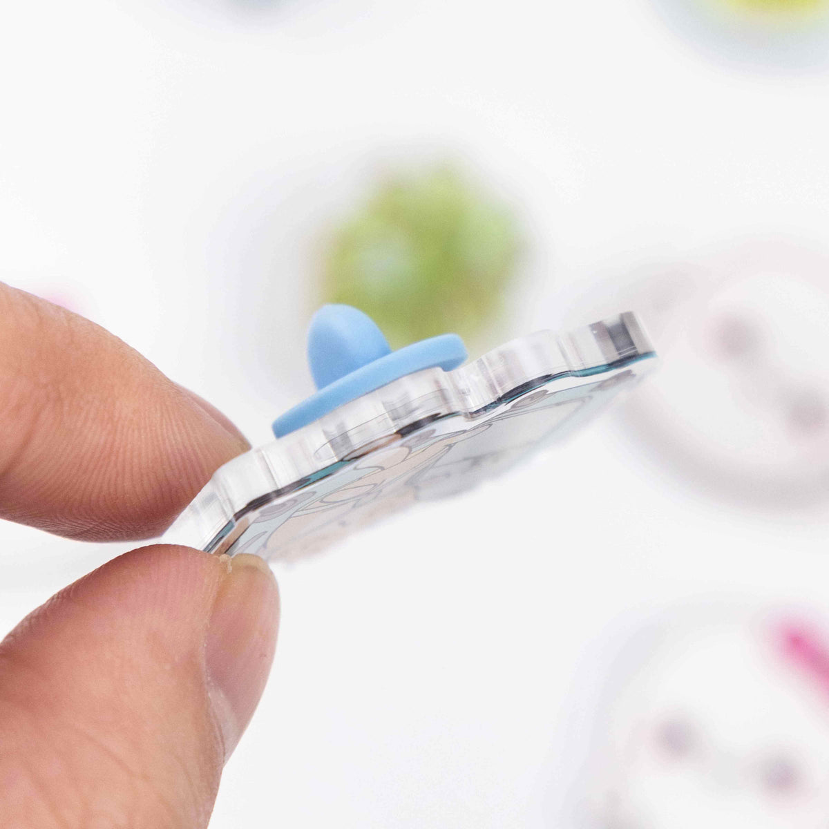 Side close‑up of clear acrylic pin, thick transparent material with blue rubber pin back, custom kawaii brooch