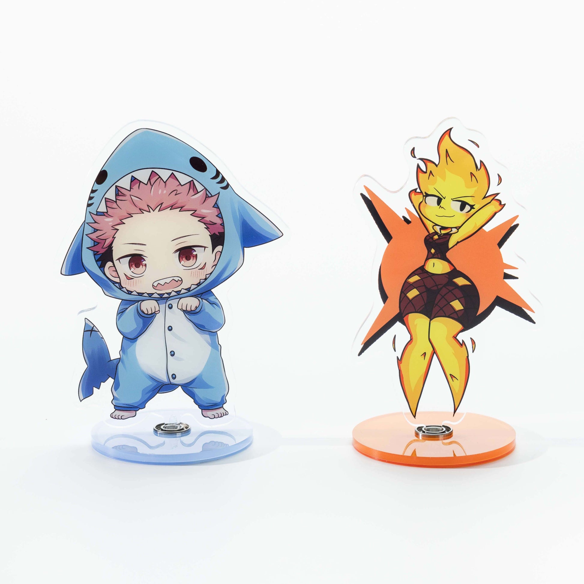 Two adorable, custom acrylic rotating standees featuring chibi anime characters—a boy in a shark onesie and a flame girl—designed as anime-themed desktop ornaments.