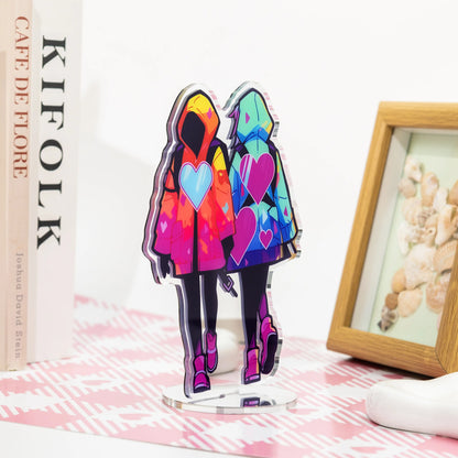 Colorful hooded couple character mirror acrylic standee, anime desk display decor on pink‑white patterned table